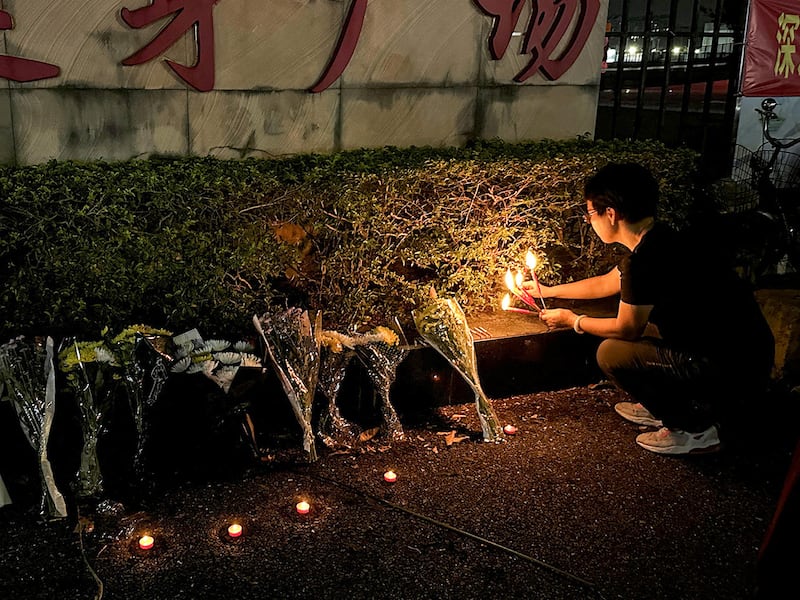 A woman lights candles near floral tributes outside a sports center, Nov. 12, 2024, in Zhuhai, China, where a car ran into a crowd of people.