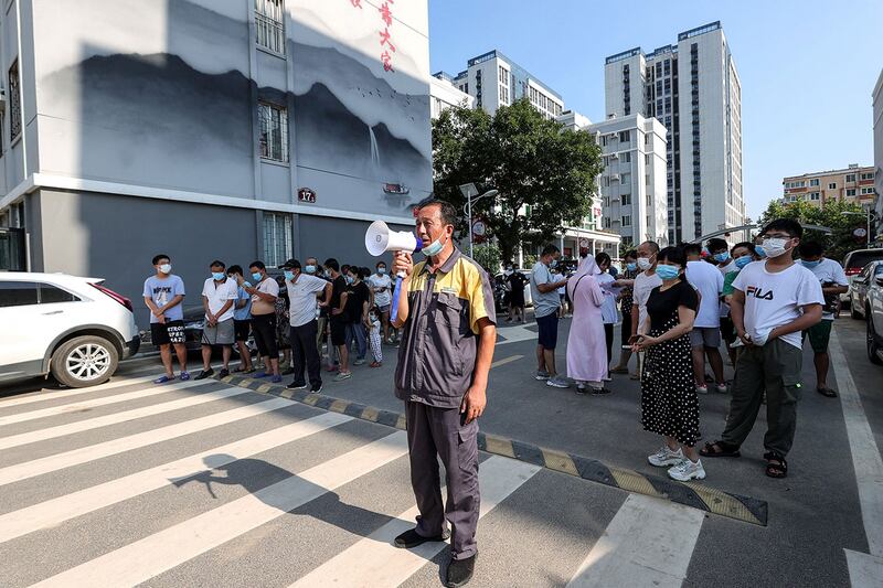 2021年7月31日，一名男子在郑州通过扬声器维持秩序，居民排队接受新冠核酸检测。