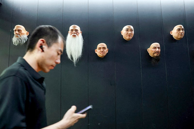 An employee checks his mobile phone as he walks past displays of robot heads in Dalian, Liaoning province, China June 6, 2024. (Florence Lo/Reuters)