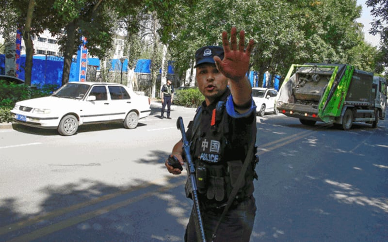 A Chinese police officer armed with an automatic weapon gestures towards reporters at a roadblock near what is officially called a vocational education center for Uyghurs in Ghulja in northwestern China's Xinjiang region, Nov. 29, 2018. Credit: Reuters