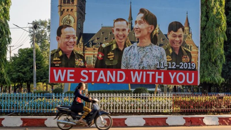 A motorcyclist rides past a billboard depicting Myanmar State Counselor Aung San Su Kyi with the three military ministers against the backdrop of the UN's International Court of Justice, displayed along a road in Hpa-an, southeastern Myanmar's Kayin state, Nov. 28, 2019. 