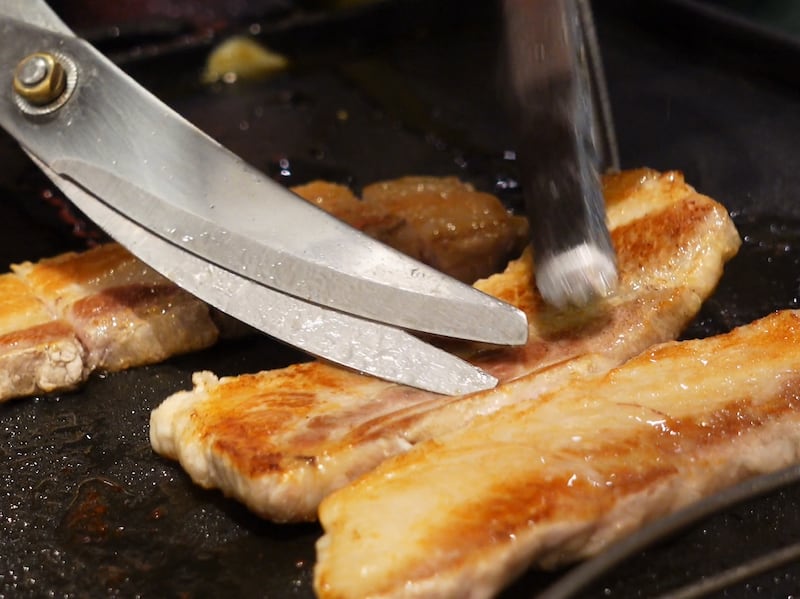 Scissors are used to cut pork belly at a Korean barbecue restaurant.