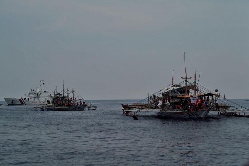 A Philippine Coast Guard ship is seen in the background as boats belonging to a civilian convoy sail toward Scarborough Shoal in the South China Sea, May 15, 2024. (Jojo Riñoza/BenarNews)