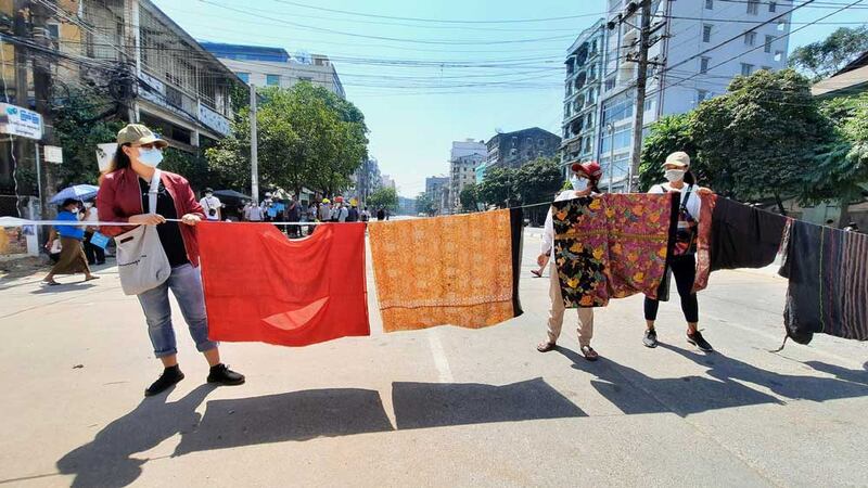 Women in Tamwe, Yangon, prepare to raise a line of sarongs to frustrate security forces. Myanmar superstition holds that walking beneath women's sarongs is bad luck or shameful for men. (RFA)