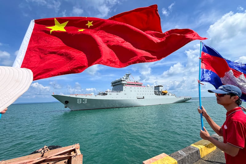 People wave Cambodian and Chinese flags as the Chinese ship Qi Jiguang prepares to dock with a banner reading "Bring peace and friendship to meet good friends" at the Sihanoukville port, May 19, 2024.