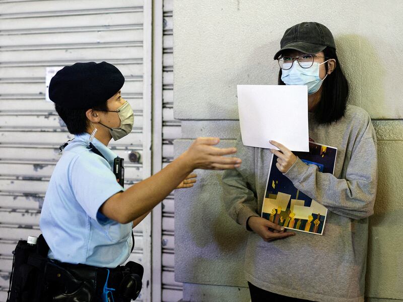 A police officer asks a woman to leave as she holds white sheets of paper during a commemoration of the victims of a fire in Urumqi, in Hong Kong Kong, China November 28, 2022.