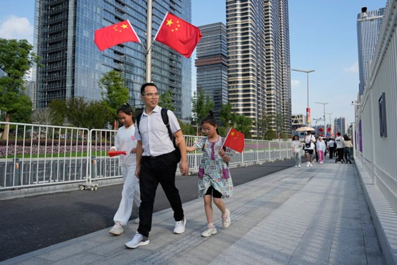 A family walks with Chinese flags as the country marks its 74th National Day in Hangzhou, China, Oct. 1, 2023. (Aaron Favila/AP)